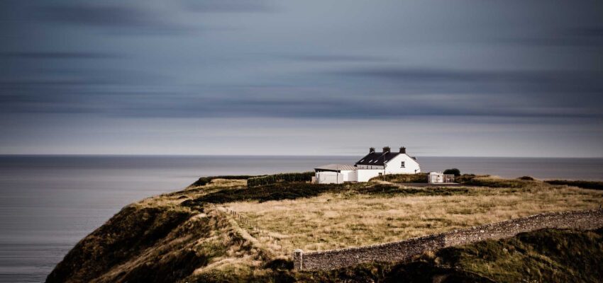 Maison isolée sur falaise avec vue sur mer.