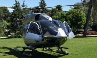 Hélicoptère stationné sur herbe avec arbres derrière.